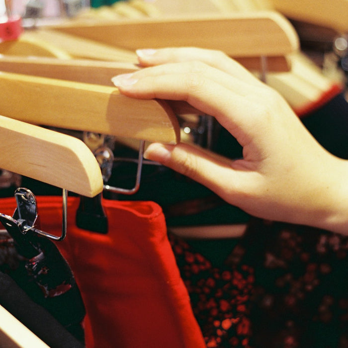 Hand reaching along a rail of wooden clothing hangers